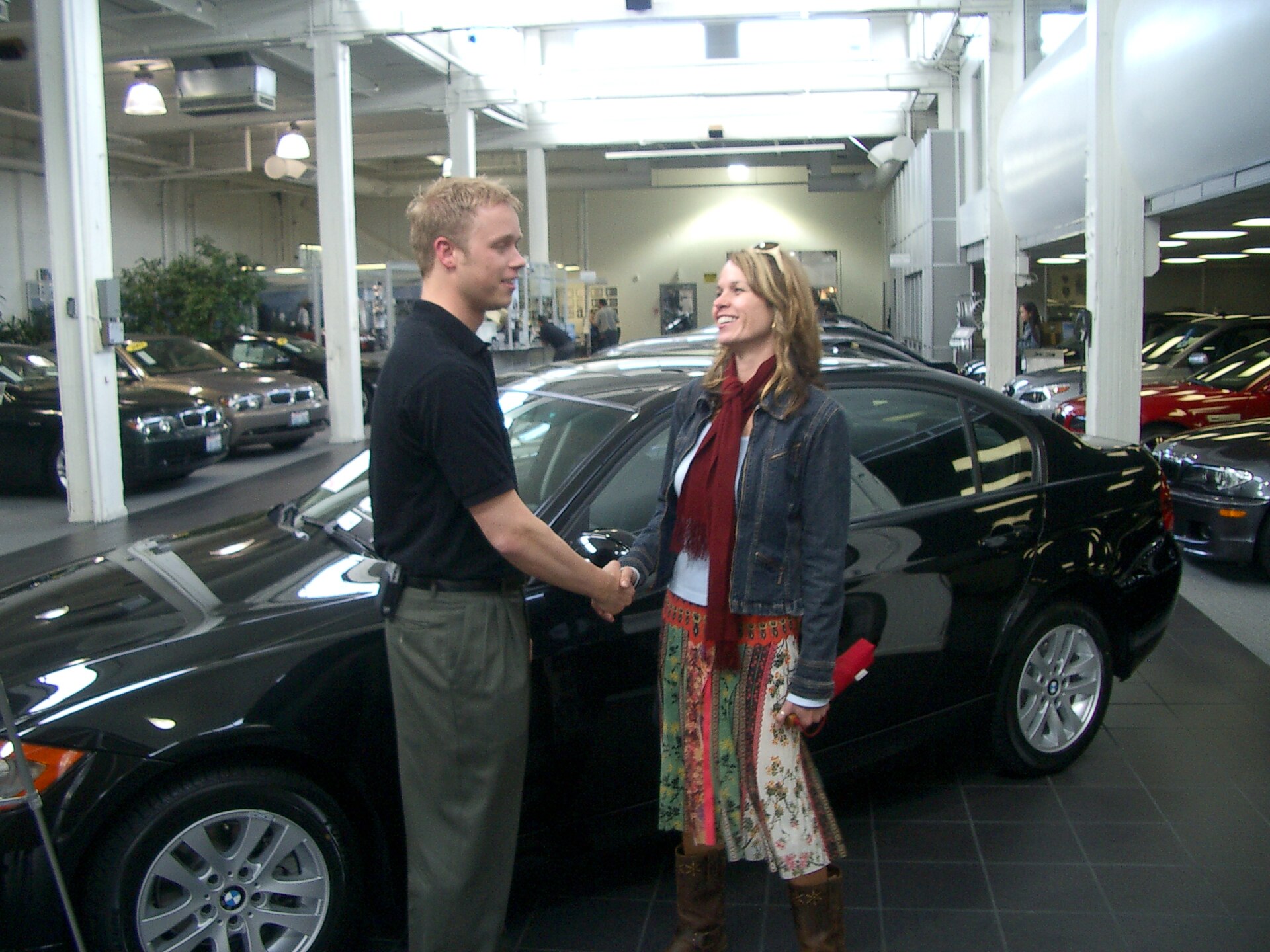 Team member shaking hands with a new car salesman in front of a new car